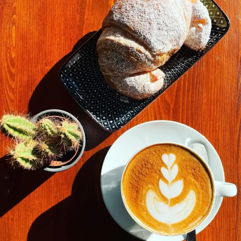 Colazione L'Estro con cappuccino, specialty coffee e dolce e salato a scelta Cappuccino con latte art, croissant, brioche, su tavolo in legno per una colazione dolce all'Estro dalle 7.30 fino a tarda notte